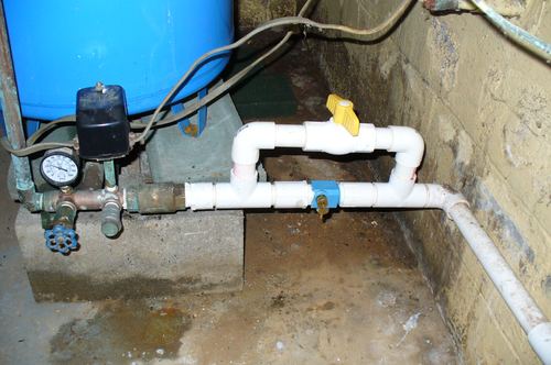 Well pressure tank, pump pressure switch, and shutoff valves installed in a basement corner