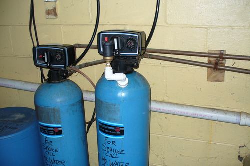 Two water softener and acid neutralizer tanks installed side by side with a Mr. Water LLC service tag