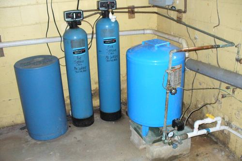 Water softener, acid neutralizer, and well pressure tank installed together in a basement corner
