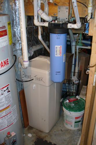 Whole-house carbon filter mounted above a brine tank next to a propane water heater