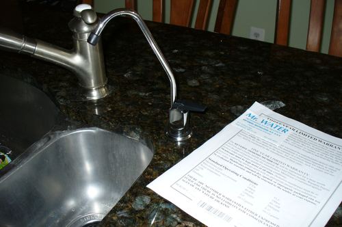 Close-up of a reverse osmosis drinking water faucet with warranty paperwork
