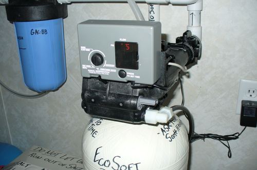 Close-up of a water softener control valve with a carbon filter mounted nearby