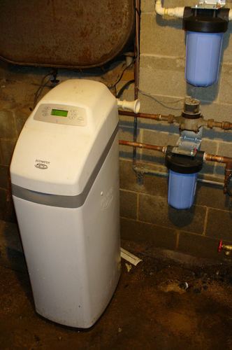 Older rusted tank next to an EcoWater water softener with dual whole-house filters